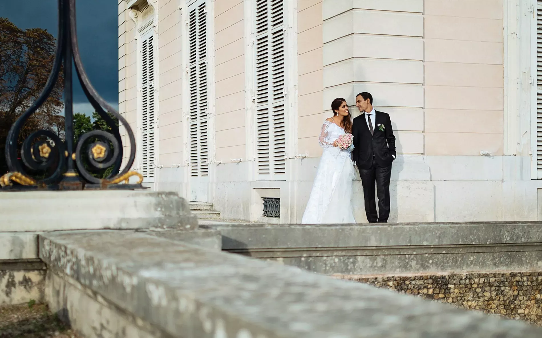 Séance photo de mariage en extérieur par TRIFA Studio, mettant en scène un couple de mariés élégant et radieux. La mariée, vêtue d'une robe blanche fluide, et le marié, en costume chic, posent avec tendresse dans un cadre naturel idyllique. Le décor, baigné de lumière dorée, offre une atmosphère romantique et intemporelle, sublimée par l'expertise de TRIFA Studio en photographie de mariage. Découvrez des clichés uniques qui capturent l'amour et l'émotion authentique.